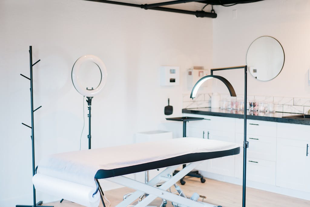 Contact botox clinic. Bright and modern medical spa room featuring massage bed and studio lighting.